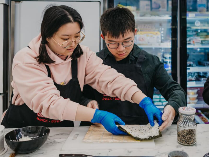 A woman helping a man making handmade sushi